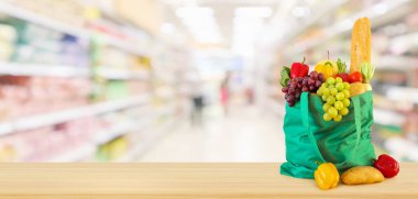 Yeniden kullanılabilir yeşil alışveriş poşetinde taze meyve ve sebzeler. Ahşap masanın üzerinde. Marketin arka planı bulanıklaşmış.