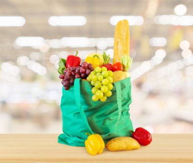 Yeniden kullanılabilir yeşil alışveriş poşetinde taze meyve ve sebzeler ahşap masanın üstünde süpermarket bakkalının bokeh ışıklı bulanık arka planıyla