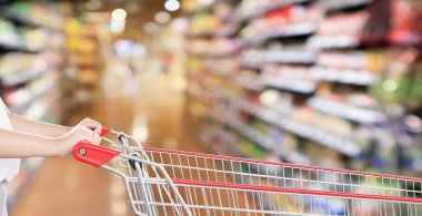 Kadın alışveriş arabasının arka planında bulanık süpermarket rafları var.