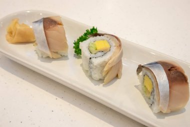 Saba suşisi beyaz tabakta yuvarlanıyor.