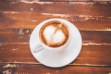 Kafe restoranındaki ahşap masada, beyaz kahve fincanında, kalp şeklinde latte sanatı.