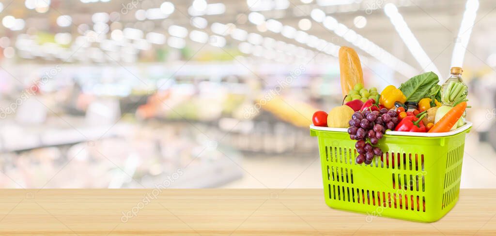 Shopping basket filled with fruits and vegetables on wood table with supermarket grocery store blurred defocused panorama background