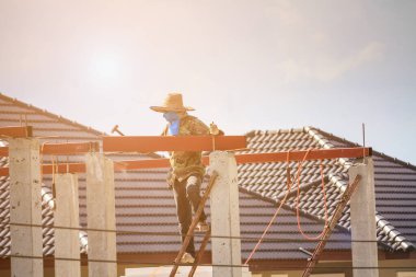 İnşaat işçileri binanın çatısının çelik iskelet yapısını inşa ediyorlar. İnşaat alanında bulutlar ve gökyüzü var.