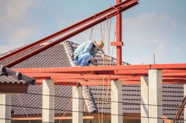 İnşaat işçileri binanın çatısının çelik iskelet yapısını inşa ediyorlar. İnşaat alanında bulutlar ve gökyüzü var.