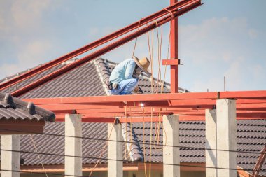 İnşaat işçileri binanın çatısının çelik iskelet yapısını inşa ediyorlar. İnşaat alanında bulutlar ve gökyüzü var.