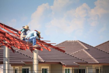 İnşaat işçileri binanın çatısının çelik iskelet yapısını inşa ediyorlar. İnşaat alanında bulutlar ve gökyüzü var.