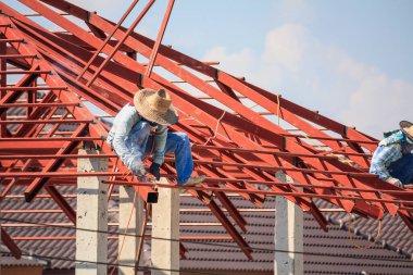 İnşaat işçileri binanın çatısının çelik iskelet yapısını inşa ediyorlar. İnşaat alanında bulutlar ve gökyüzü var.
