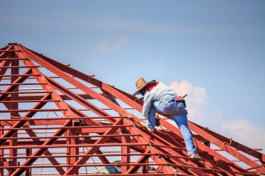 İnşaat işçileri binanın çatısının çelik iskelet yapısını inşa ediyorlar. İnşaat alanında bulutlar ve gökyüzü var.