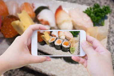 Cep telefonu kullanan bir kadın Japon suşi setinin fotoğrafını çekiyor.