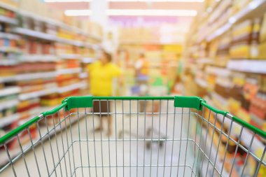 Süpermarket koridorlu alışveriş arabası. Arka plan bulanık süpermarketten alışveriş yapan insanlarla dolu.