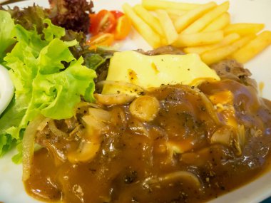 Peynirli ızgara biftek, yanında patates kızartması ve beyaz tabakta sebze.