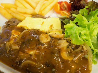 Peynirli ızgara biftek, yanında patates kızartması ve beyaz tabakta sebze.