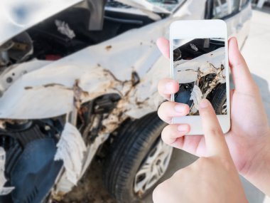 Cep telefonu kullanan bir kadın sigorta için araba kazası hasarının fotoğrafını çekiyor.