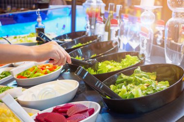 Salata büfesi restoranında sebze malzemesi seçen Asyalı kadın.