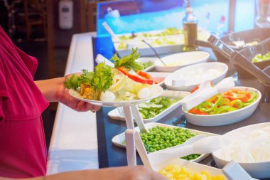 Salata büfesi restoranında sebze malzemesi seçen Asyalı kadın.