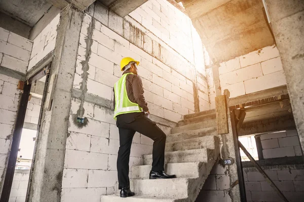 Genç profesyonel mühendis koruyucu miğfer ve bina şantiyesinde elinde proje kağıtları ile çalışıyor.