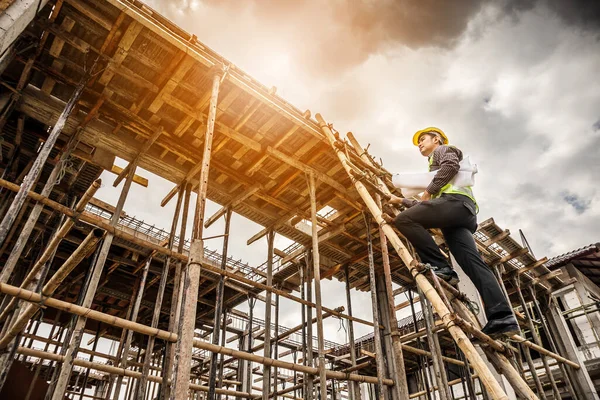 Genç profesyonel mühendis koruyucu miğfer ve bina inşaatında merdiven üzerinde çalışan planlar üzerinde çalışıyor.