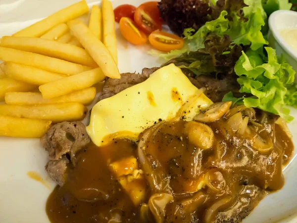 Peynirli ızgara biftek, yanında patates kızartması ve beyaz tabakta sebze.