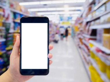 Kadın süpermarkette alışveriş yaparken cep telefonunu tutuyor.