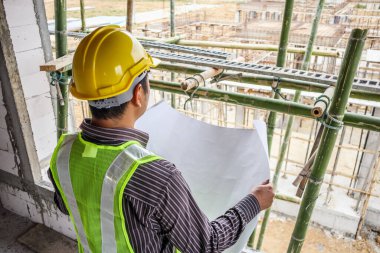 Asyalı işadamı inşaat mühendisi koruyucu miğfer ve bina inşaatında kullanılacak planlar.