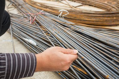 Asyalı işadamı inşaat mühendisi koruyucu miğfer ve bina inşaatındaki çelik çubuklara bakan bina planı kağıtları.