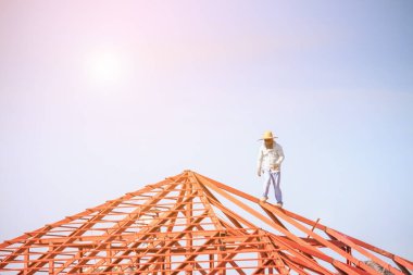 İnşaat işçileri binanın çatısının çelik iskelet yapısını inşa ediyorlar. İnşaat alanında bulutlar ve gökyüzü var.