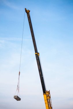 Mobil inşaat vinç kamyonunun sarı teleskopik kolları inşaat alanındaki inşaat alanına beton levha kaldırıyor.