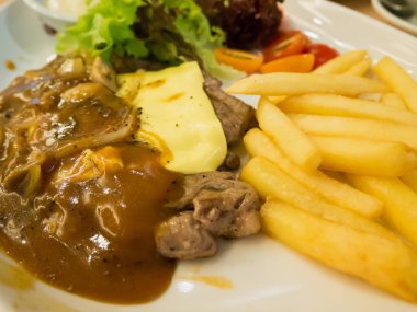 Peynirli ızgara biftek, yanında patates kızartması ve beyaz tabakta sebze.