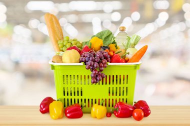 Tahta masanın üzerinde meyve ve sebzelerle dolu alışveriş sepeti. Marketin arka planında bulanıklık var.