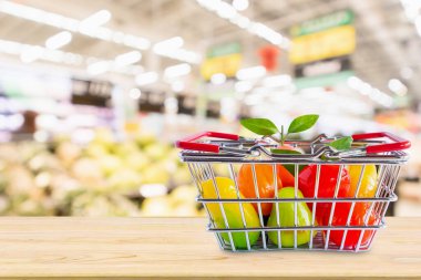 Marketin arka planında, ahşap masada meyveli alışveriş sepeti.
