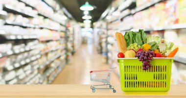 Tahta masanın üzerinde meyve ve sebzelerle dolu alışveriş sepeti. Marketin arka planında bulanıklık var.