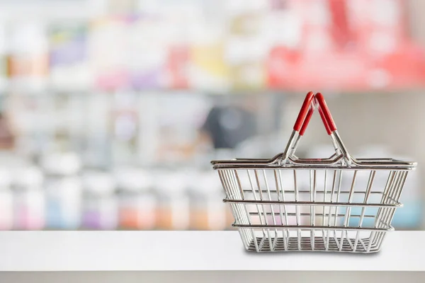 Empty shopping basket on pharmacy drugstore counter with blur shelves of medicine and vitamin supplements background