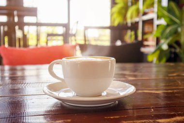 Kafe restoranındaki ahşap masada, beyaz kahve fincanında, kalp şeklinde latte sanatı.