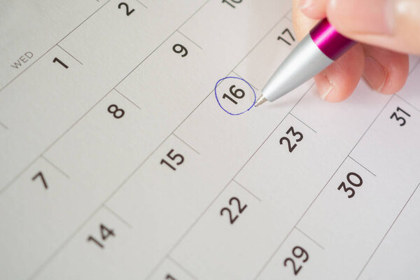 female hand holding pen circle mark on calendar page