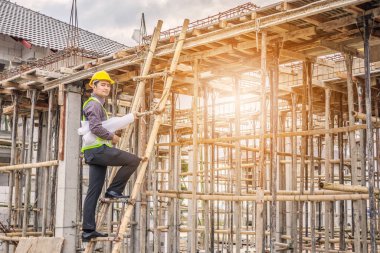 Genç profesyonel mühendis koruyucu miğfer ve bina inşaatında merdiven üzerinde çalışan planlar üzerinde çalışıyor.