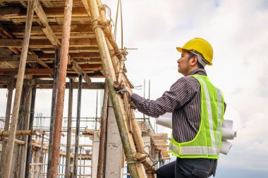 Genç profesyonel mühendis koruyucu miğfer ve bina inşaatında merdiven üzerinde çalışan planlar üzerinde çalışıyor.