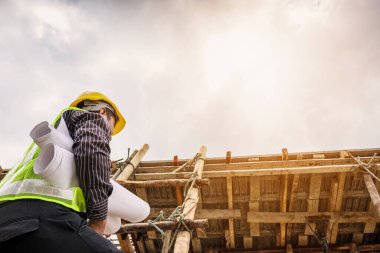 Genç profesyonel mühendis koruyucu miğfer ve bina inşaatında merdiven üzerinde çalışan planlar üzerinde çalışıyor.