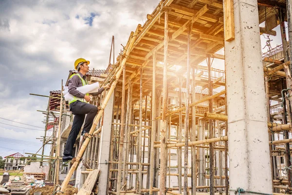 Genç profesyonel mühendis koruyucu miğfer ve bina inşaatında merdiven üzerinde çalışan planlar üzerinde çalışıyor.