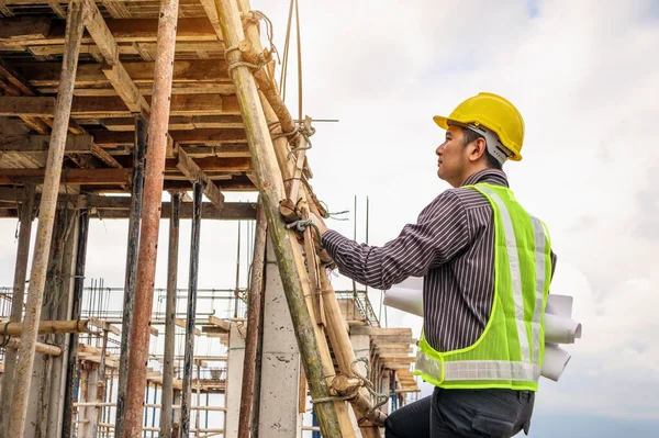 Genç profesyonel mühendis koruyucu miğfer ve bina inşaatında merdiven üzerinde çalışan planlar üzerinde çalışıyor.