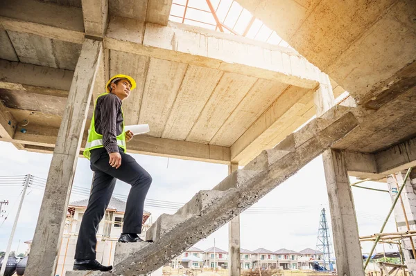 Genç profesyonel mühendis koruyucu miğfer ve bina şantiyesinde elinde proje kağıtları ile çalışıyor.