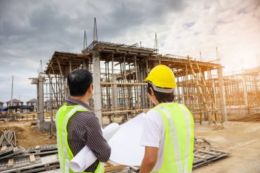 Asyalı işadamı inşaat müdürü ve koruyucu miğfer mühendisi bina inşaatında elinde planlar tutuyor.