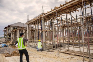 Asyalı işadamı inşaat müdürü ve koruyucu miğfer mühendisi inşaat alanının planlarını ellerinde tutuyorlar.