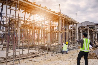 Asyalı işadamı inşaat müdürü ve koruyucu miğfer mühendisi inşaat alanının planlarını ellerinde tutuyorlar.