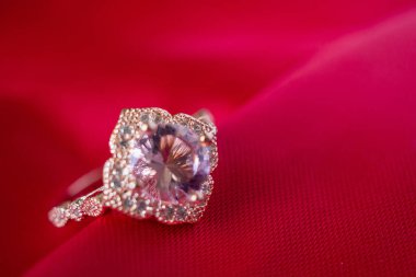 Kırmızı kumaş arkaplanda safir değerli taşlı lüks pembe mücevher yüzüğü.