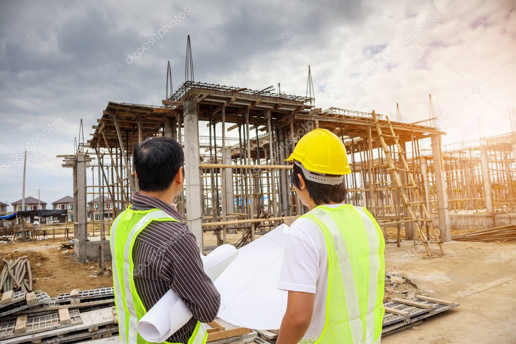 Asian business man construction manager and engineer worker in protective helmet hold blueprints paper on hand at house building site