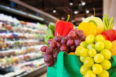 Yeniden kullanılabilir yeşil alışveriş poşetinde taze meyve ve sebzeler süpermarkette bulanık arka planda bokeh ışığı ile bulanık