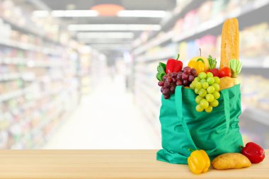 Yeniden kullanılabilir yeşil alışveriş poşetinde taze meyve ve sebzeler ahşap masanın üstünde süpermarket bakkalının bokeh ışıklı bulanık arka planıyla