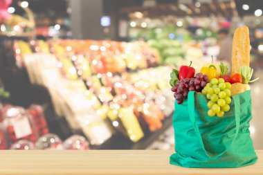 Yeniden kullanılabilir yeşil alışveriş poşetinde taze meyve ve sebzeler ahşap masanın üstünde süpermarket bakkalının bokeh ışıklı bulanık arka planıyla