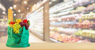 Yeniden kullanılabilir yeşil alışveriş poşetinde taze meyve ve sebzeler ahşap masanın üstünde süpermarket bakkalının bokeh ışıklı bulanık arka planıyla