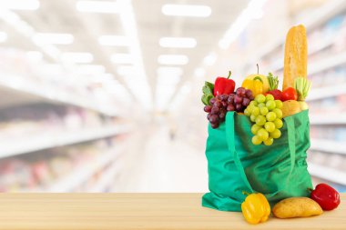 Yeniden kullanılabilir yeşil alışveriş poşetinde taze meyve ve sebzeler ahşap masanın üstünde süpermarket bakkalının bokeh ışıklı bulanık arka planıyla